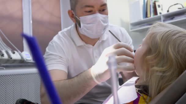 Der Zahnarzt in der Maske überprüft die Zähne eines kleinen Mädchens — Stockvideo