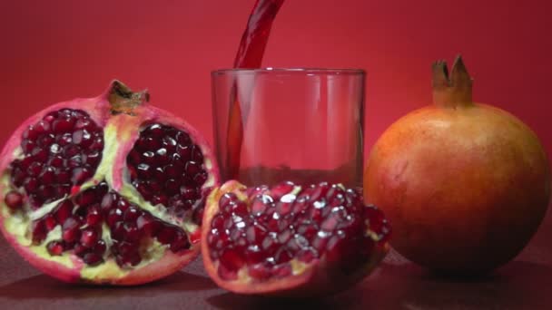 Delicioso suco de romã está fluindo em vidro ao lado das romãs maduras — Vídeo de Stock