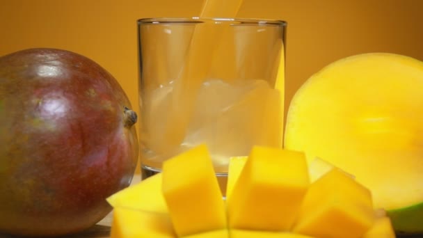 芒果汁倒入黄色背景的大成熟芒果旁边的杯子中 — 图库视频影像