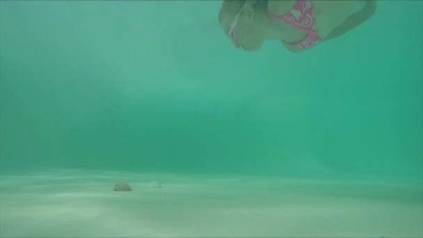 Крупный план маленькой девочки, плавающей под водой на дне бассейна — стоковое видео
