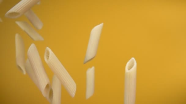 Suché syrové těstoviny penne létání diagonálně na žlutém pozadí — Stock video