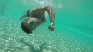 Çocuk suyun altında yüzüyor ve dönüyor.