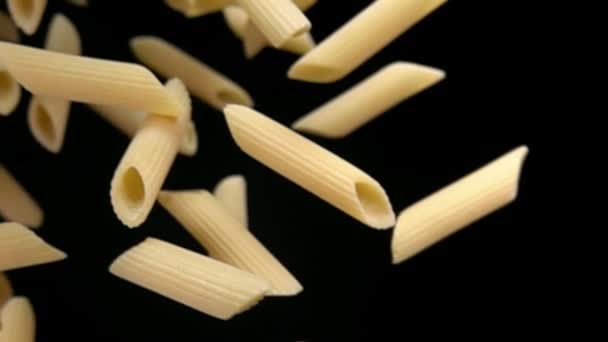 Droge rauwe pasta penne diagonaal vliegend op een zwarte achtergrond — Stockvideo