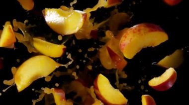 Şeftalinin dilimleri siyah arkaplanda meyve suyu damlalarıyla zıplıyor.