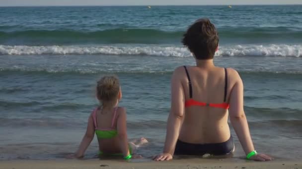 Madre e figlia sono sedute insieme e guardano le onde del mare — Video Stock