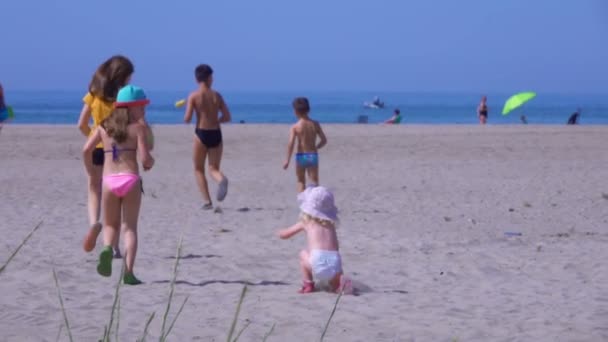 Vijf kinderen in heldere kleren rennen over het zand naar de zee. — Stockvideo