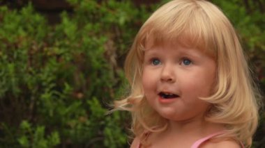 Küçük sarışın kız gülümsüyor ve elleri şaşkın bir şekilde ağzını kapıyor.