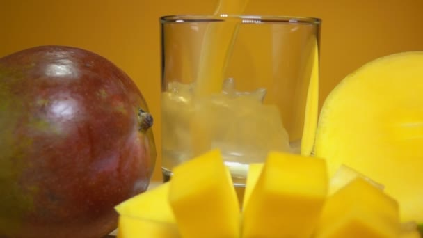 Χύνεται χυμός μάνγκο σε ποτήρι δίπλα σε μεγάλο ώριμο μάνγκο κομμένο σε κύβους — Αρχείο Βίντεο