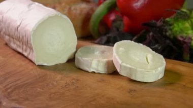 Kalın bir parça Sainte Maure de Touraine keçi peyniri tahtaya düşer.