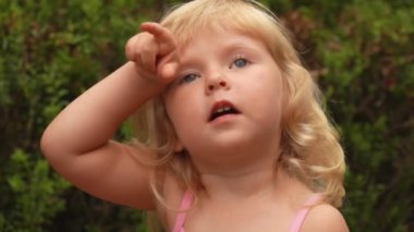 Küçük sarışın kız gökyüzüne bakıyor ve parmağıyla bir şey gösteriyor.