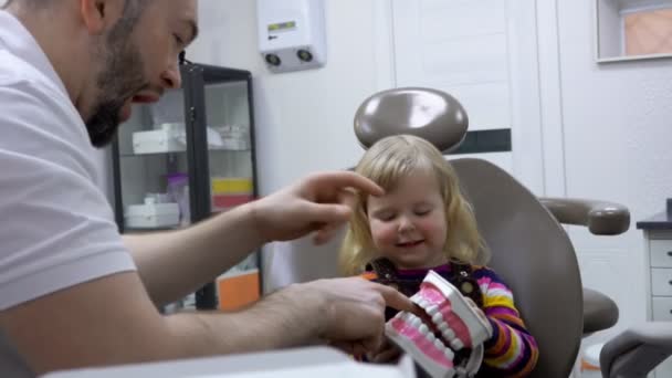 El dentista le explica a una niña cómo limpiar los dientes en un modelo de mandíbula de plástico — Vídeo de stock