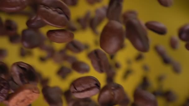 Close-up van gebrande koffiebonen die diagonaal op de gele achtergrond vliegen — Stockvideo