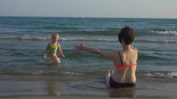 Een klein meisje rent naar haar moeder aan de kust door de zee golven — Stockvideo