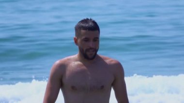 Genç yakışıklı adam deniz sörfünün suyundan çıkıyor.