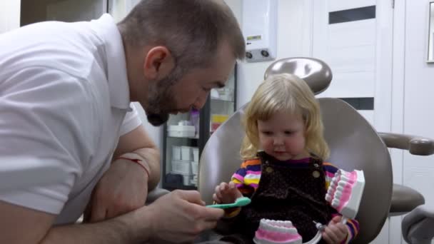 Dokter gigi menjelaskan kepada seorang gadis kecil bagaimana membersihkan giginya dengan sikat gigi — Stok Video