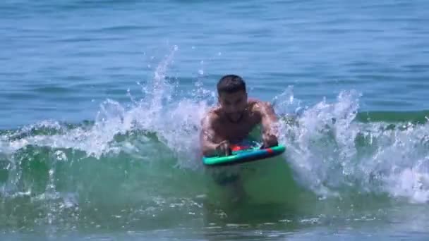 Joven hombre guapo está nadando en el tablero en las olas del mar surf — Vídeos de Stock