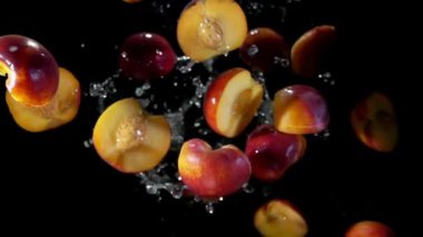 Şeftalinin yarısı siyah arkaplanda su damlalarıyla zıplıyor.