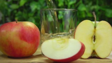 Taze elma suyu yeşil çalılığın arka planındaki bir bardağa dökülür.