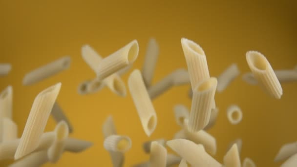 Primer plano de la pasta cruda penne volando hacia arriba y girando sobre un fondo amarillo — Vídeo de stock