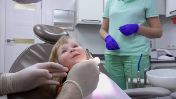 De tandarts vraagt een schattig klein meisje om de mond te openen en haar tanden te laten zien — Stockvideo