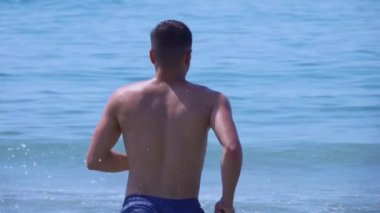 Genç yakışıklı adam deniz dalgalarına doğru koşuyor.