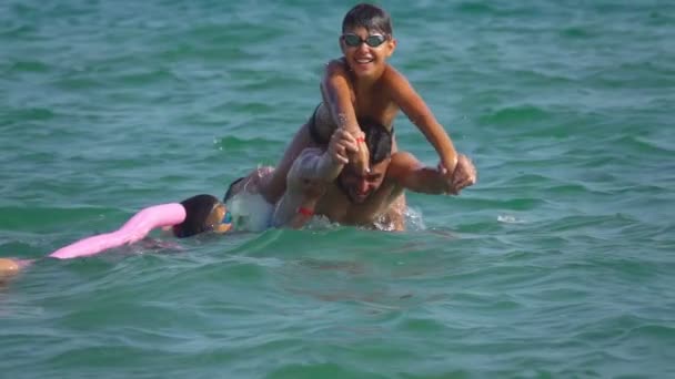 El joven está jugando con los niños en el agua de mar y ayudándoles a bucear — Vídeos de Stock