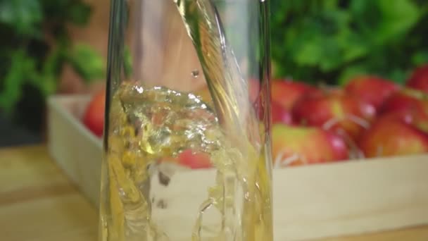Appelsap wordt in de kan gegoten op de achtergrond van een mand vol appels — Stockvideo