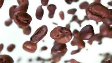 Beyaz arka planda çapraz uçan kavrulmuş kahve çekirdekleri yakın plan.