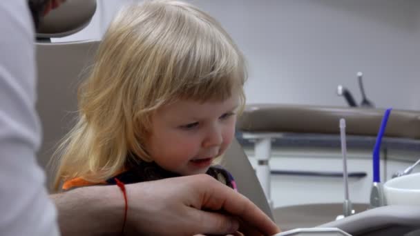 Dokter gigi menjelaskan kepada seorang gadis kecil ceria bagaimana membersihkan giginya — Stok Video