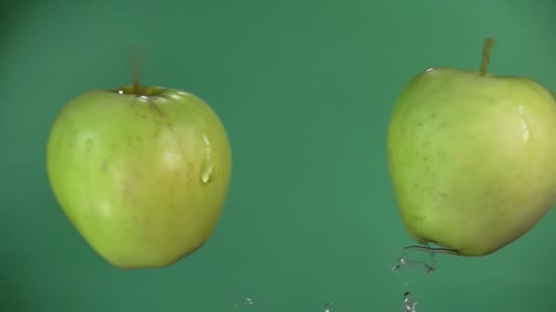 Twee appels botsen en verhogen spatten water op de groene achtergrond — Stockvideo