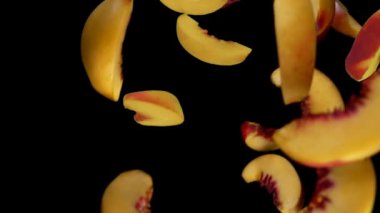 Taze olgun şeftalinin dilimleri siyah arka fona çapraz düşüyor.