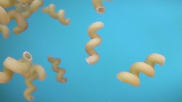 Close-up van droge pasta cellentani die diagonaal op de blauwe achtergrond valt — Stockvideo