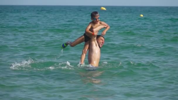 Молодой папа помогает маленькому мальчику нырнуть в морскую воду — стоковое видео