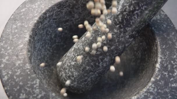 Los granos de pimienta blanca picante están cayendo en el mortero de piedra gris — Vídeos de Stock