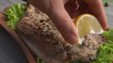 Elim leziz ızgara beyaz balık filetosuna limon suyu sıkıyor.