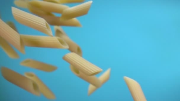 Gros plan de pâtes sèches crues penne volant en diagonale sur un fond bleu — Video