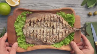 Eller masaya limonlu ızgara beyaz balık tabağı koyuyor.