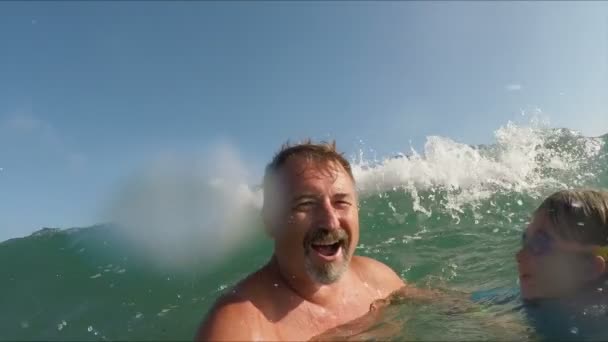Vader en een meisje in blauwe zwempakken springen in een spetterende zee golven — Stockvideo