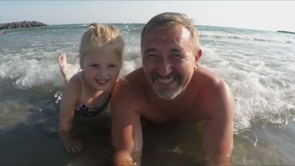 Vader en meisje liggen in een zee golven en glimlachen gelukkig — Stockvideo