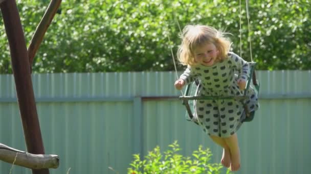 Fröhliches kleines Mädchen im grauen Kleid schwingt an einem sonnigen Tag im Freien — Stockvideo