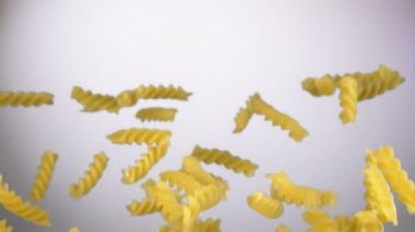 Kuru çiğ makarna fusili beyaz arka planda zıplıyor.