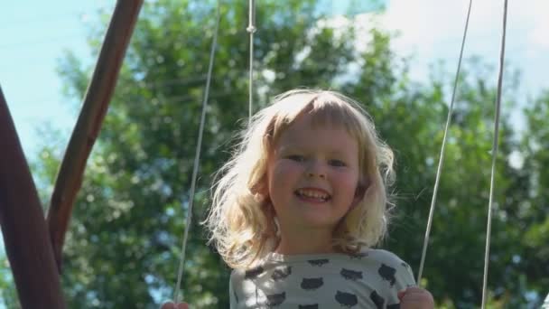 Fröhliches kleines Mädchen im grauen Kleid schwingt und lacht im Freien — Stockvideo