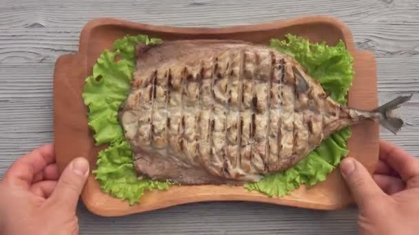 Eller masaya ızgara beyaz balık filetosu ile ahşap bir tabak koyuyor. — Stok video