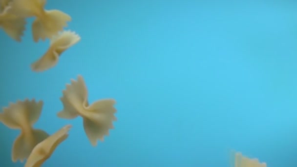 Farfalle 'ın mavi arka planda çapraz uçan kuru makarna yakın plan. — Stok video