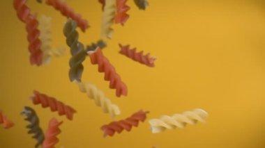 Kuru renkli makarna fusili sarı arkaplana çapraz düşüyor