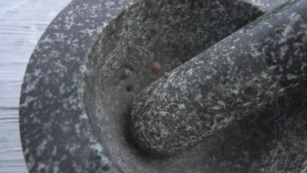 Los granos de pimienta negra están cayendo en el mortero de piedra gris — Vídeos de Stock