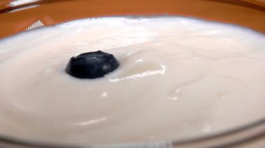 Lezzetli beyaz kremanın üzerindeki cam kaseye büyük yaban mersini düşüyor.