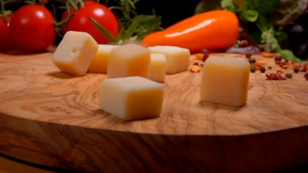 Вкусные твердые кубики сыра падают на доску на фоне помидоров — стоковое видео