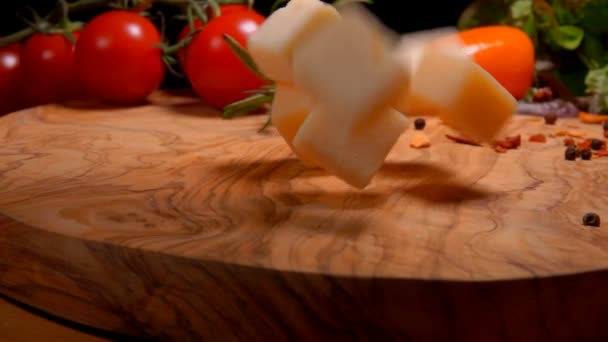 Des cubes de fromage à pâte dure tombent sur une planche de bois — Video