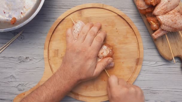 Вид зверху на руки, що пробивають сирі курячі крильця з дерев'яним шампуром — стокове відео